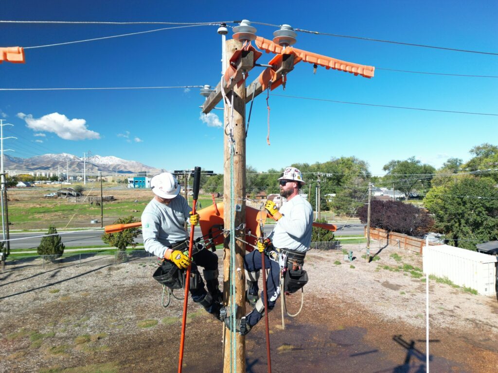 Two workers repair power lines on utility pole.