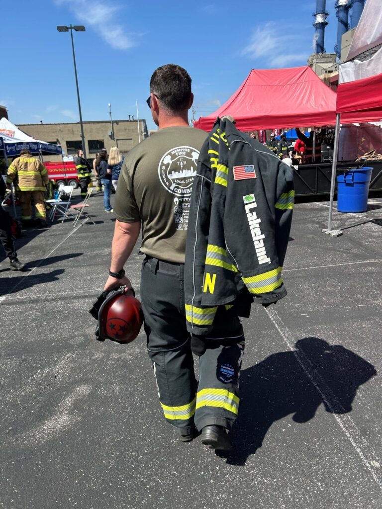 Firefighter walking at community event with jacket and helmet.